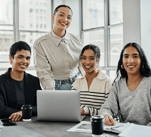 Four women smiling around a laptop.