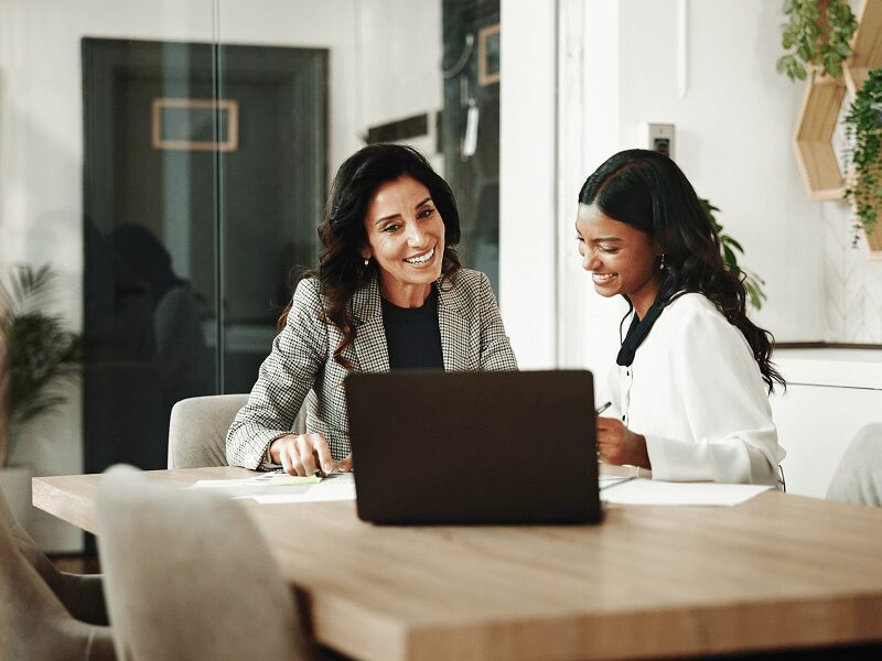 Two women smiling, working at a laptop.